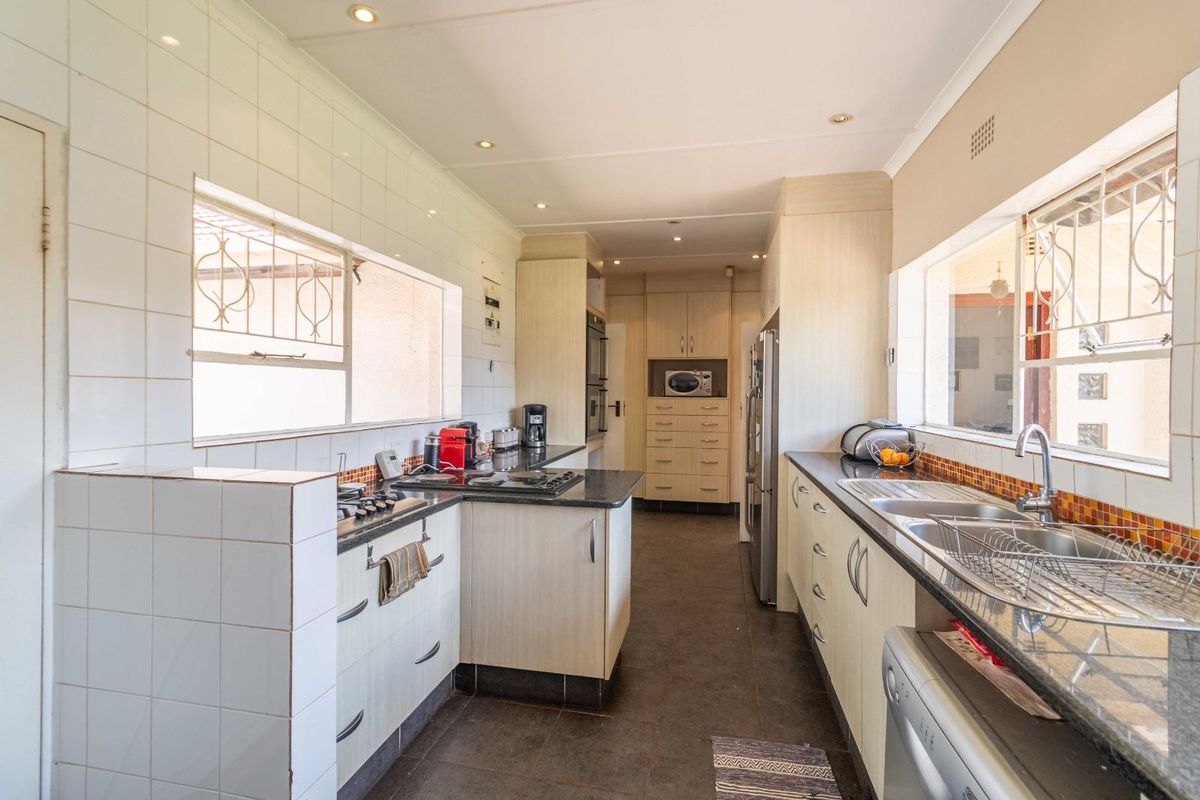 A functional galley-style kitchen featuring light wood cabinetry, dark granite countertops, built-in oven, gas hob, and double stainless steel sink.