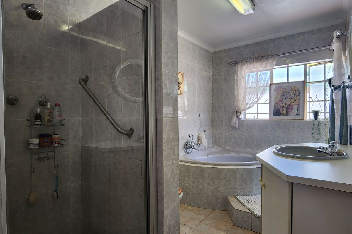 A functional bathroom featuring a built-in corner bathtub, a separate glass-enclosed shower with a grab rail, and a vanity basin.