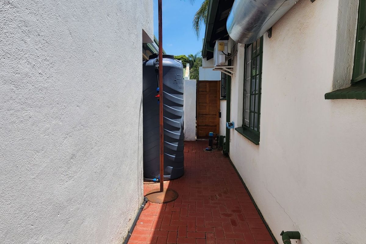 A narrow side exterior walkway featuring red brick paving, a large water storage tank, and an external air conditioning unit mounted on the wall.