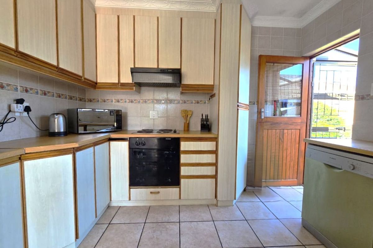 A functional kitchen featuring light-toned cabinetry, built-in oven and hob, tiled flooring, and direct access to the exterior through a wooden door.