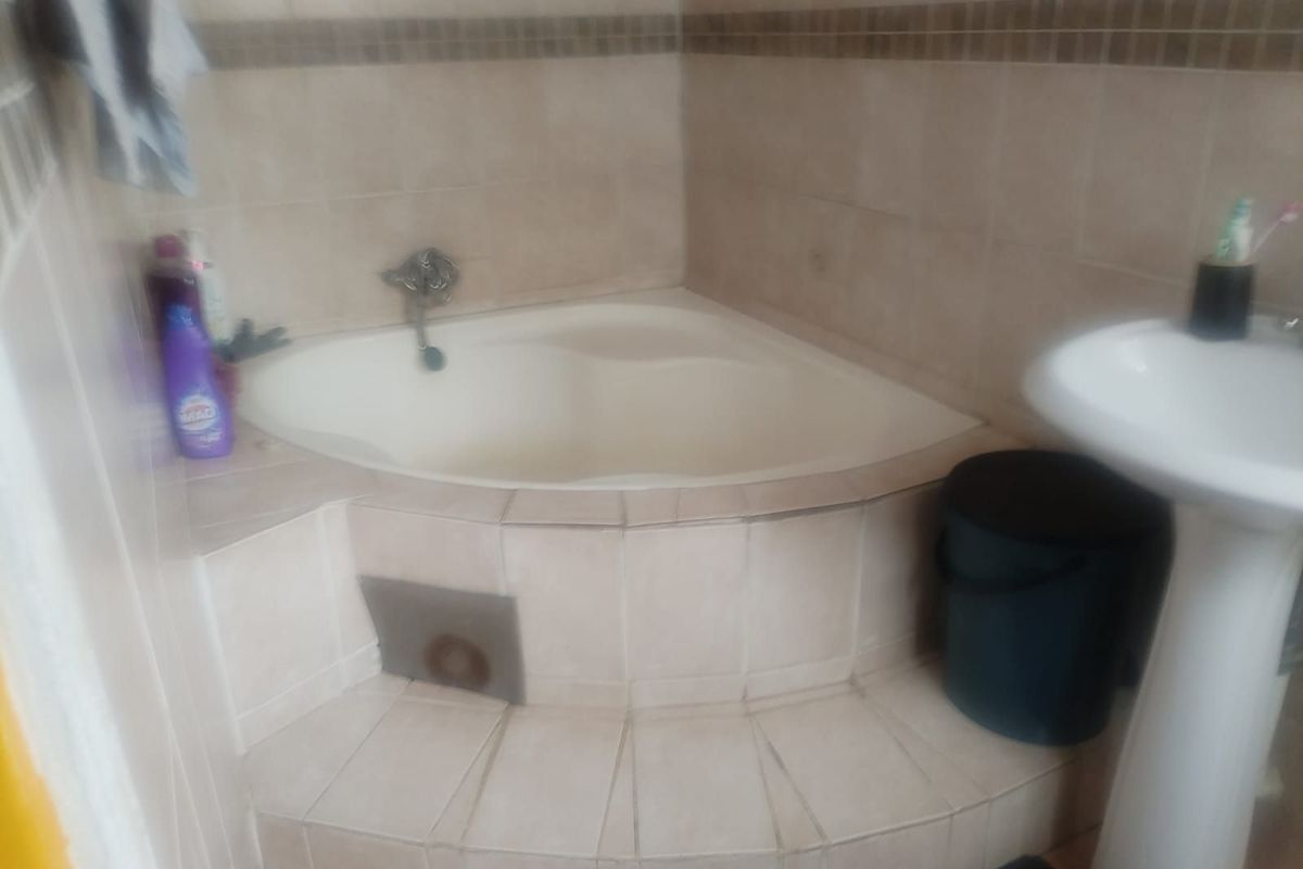A bathroom featuring a built-in corner bathtub with tiled surround and a pedestal basin.