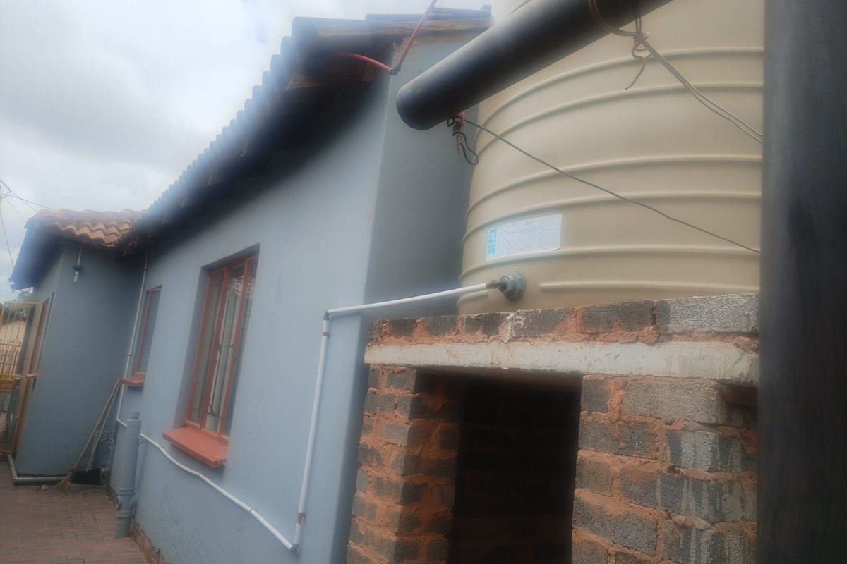 Exterior view of the property showing a water storage tank mounted on a brick plinth alongside the house wall.