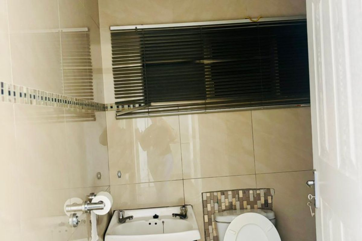 A compact bathroom featuring floor-to-ceiling wall tiles, a wall-mounted basin, and a standard toilet.
