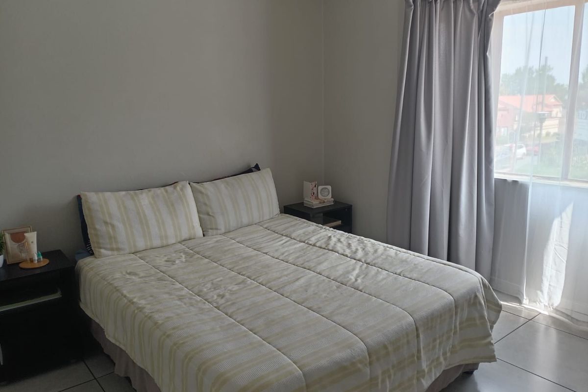 A bright bedroom featuring tiled flooring and a large window with curtains, providing natural light and a view of the exterior.