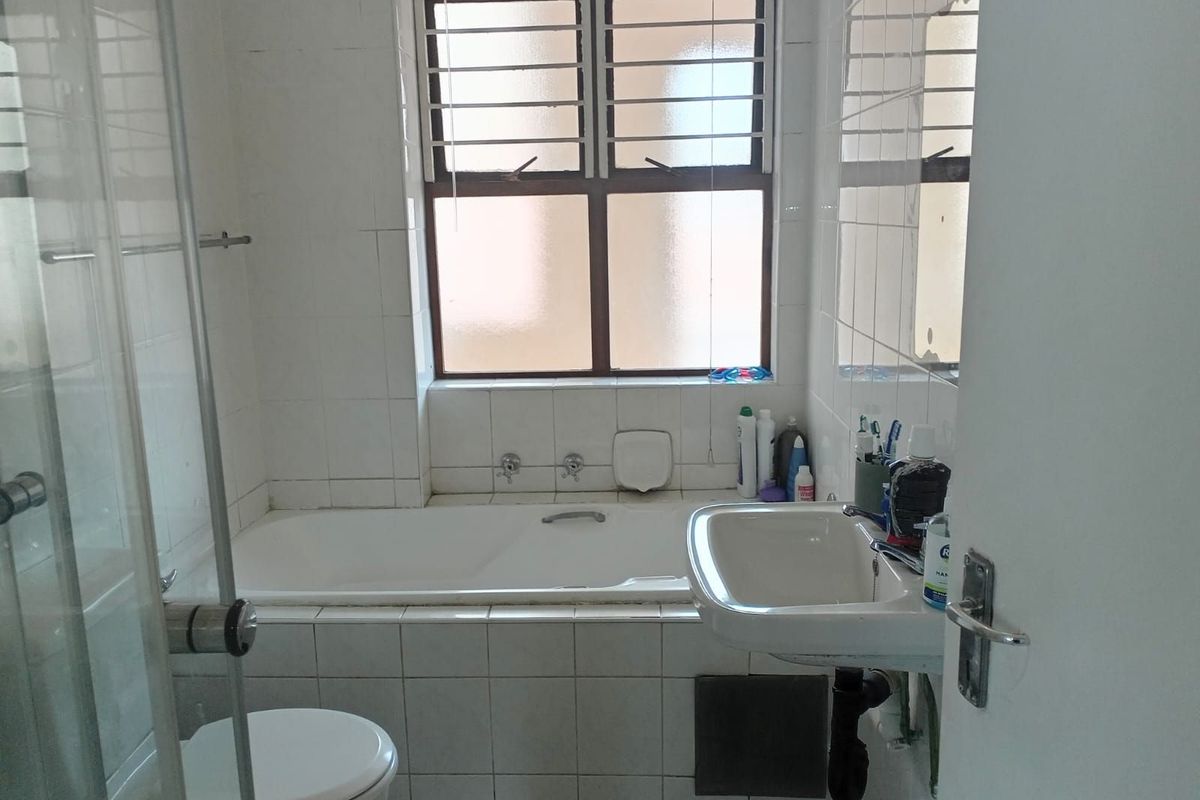 A functional bathroom featuring a built-in bathtub, wall-mounted basin, and a separate shower enclosure with tiled walls and a window for natural light.