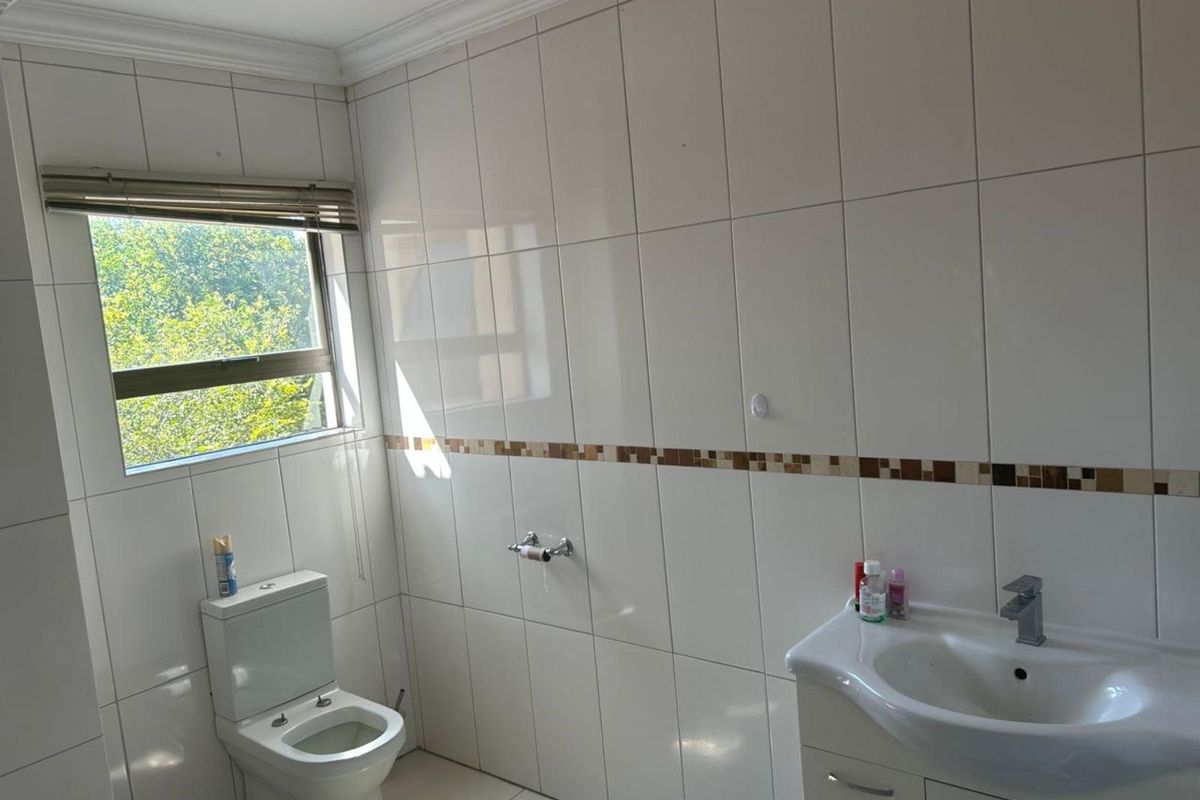 A functional bathroom featuring white wall tiles with a decorative mosaic border, a vanity basin, and a standard toilet.