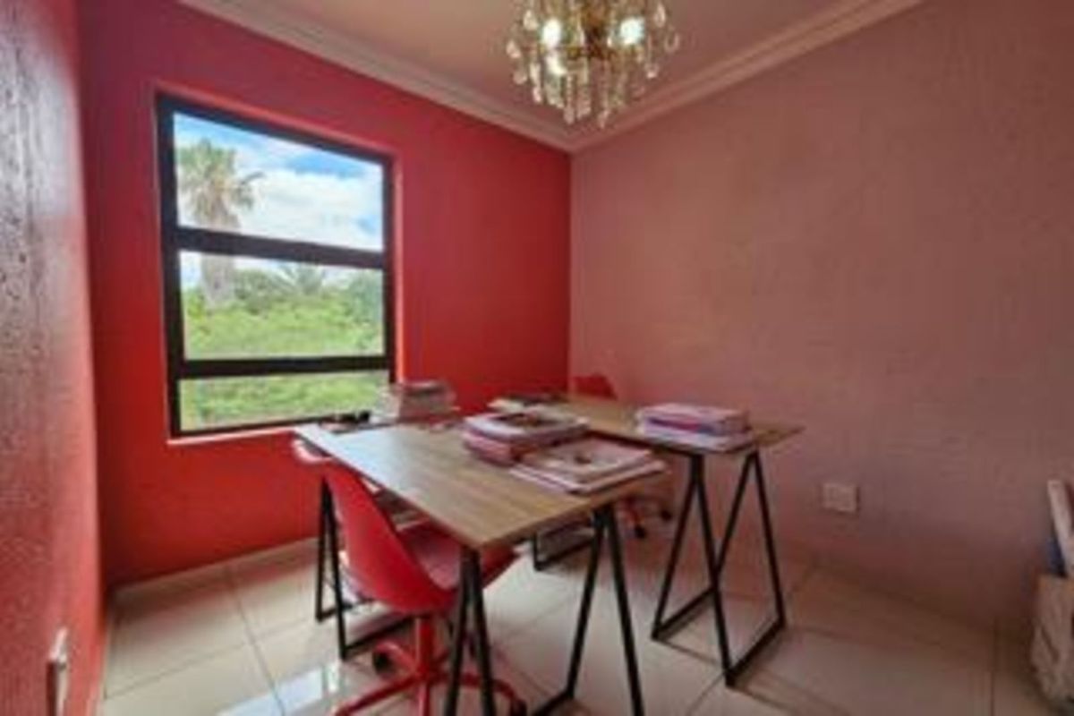 A functional bedroom or office space featuring tiled flooring, a large window with exterior views, and a decorative ceiling light fixture.