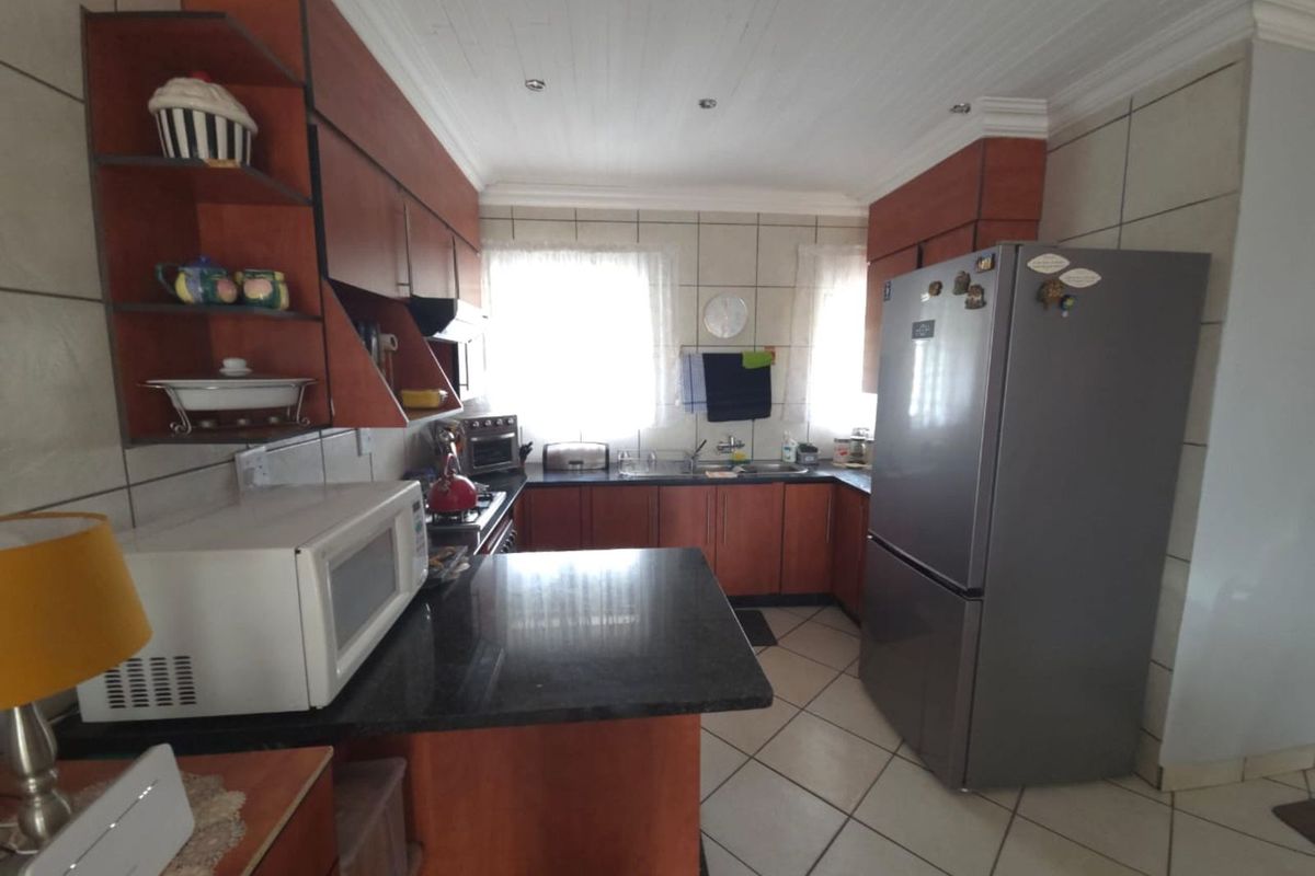 A functional kitchen featuring dark granite countertops, wood-finish cabinetry, tiled flooring, and a dedicated space for a large refrigerator.