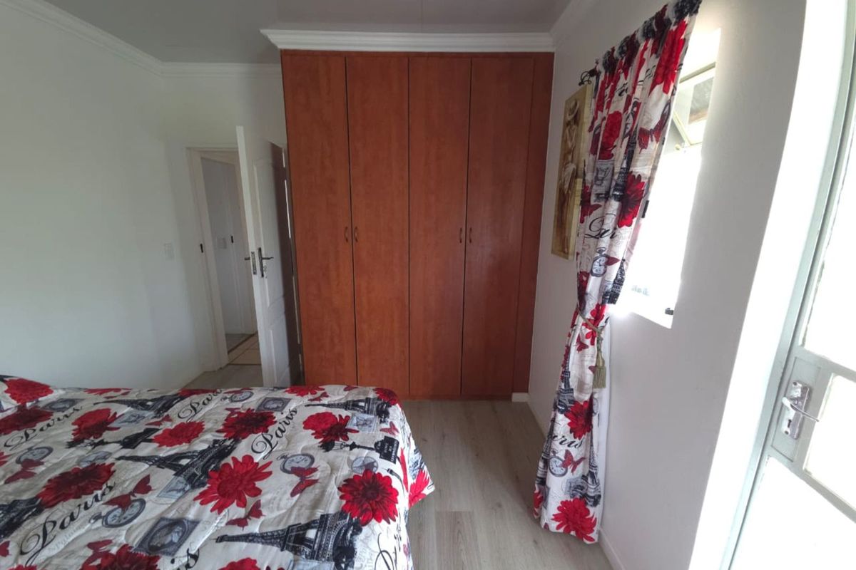 A bedroom featuring built-in wooden cupboards, light-toned laminate flooring, and a window providing natural light.