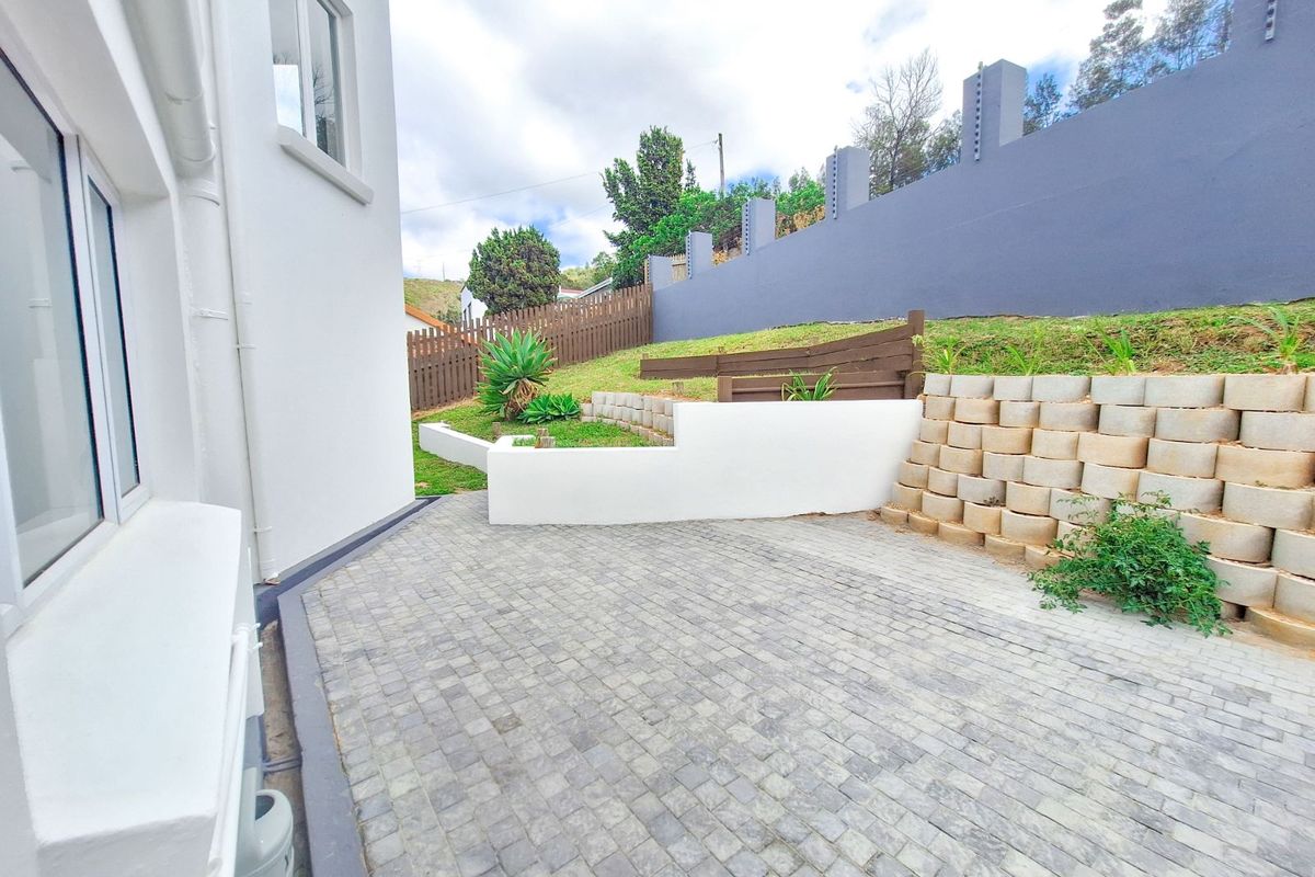 A well-maintained rear exterior area featuring paved patio space, tiered retaining walls, and a secure perimeter boundary wall.