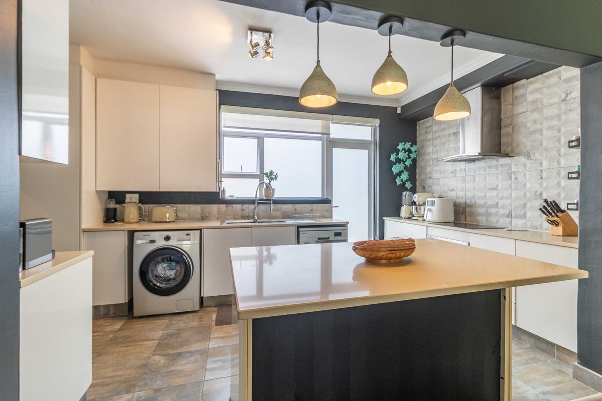 Modern kitchen featuring a central island, built-in cabinetry, integrated appliances, and tiled flooring with contemporary pendant lighting.