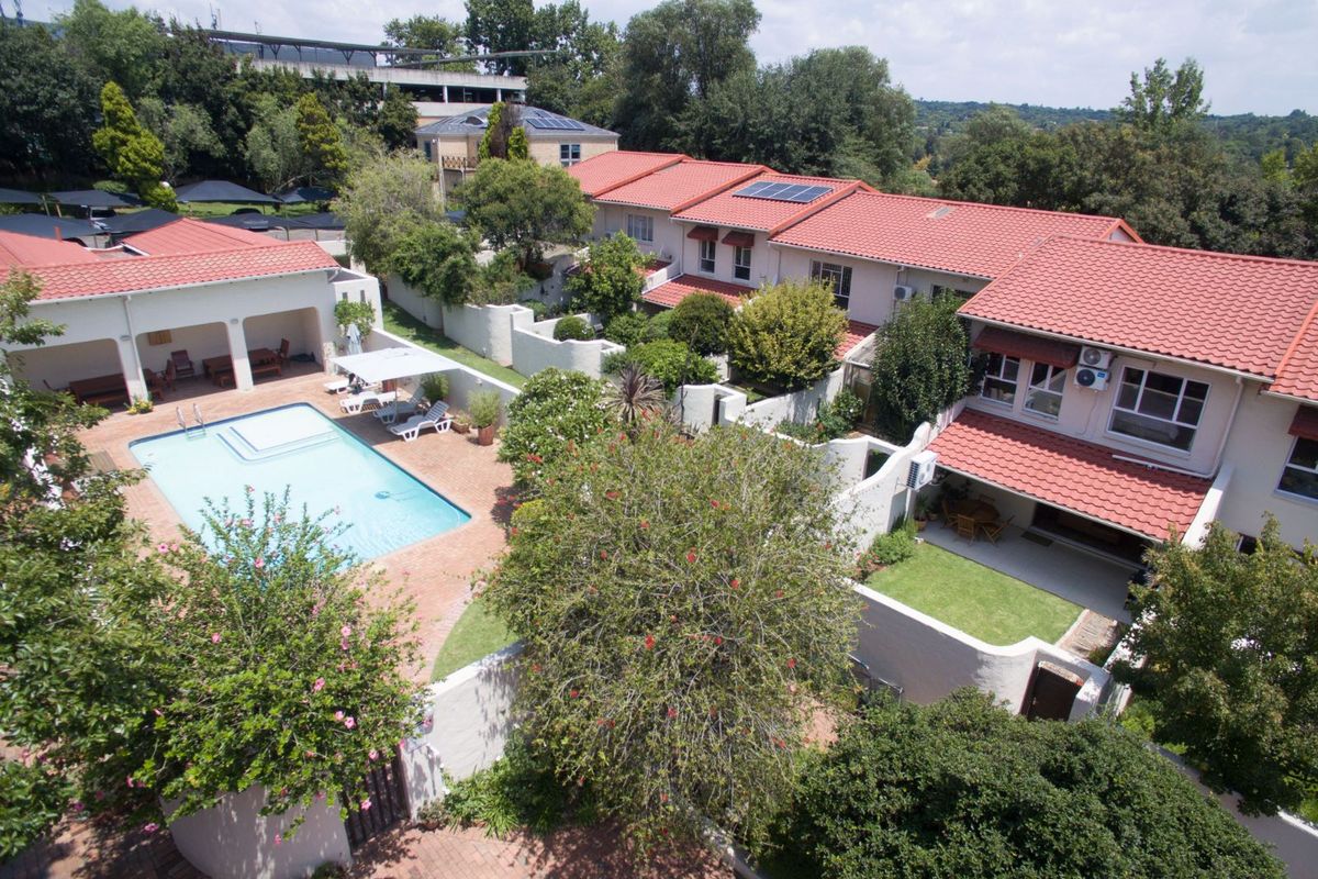 Aerial view of a residential complex featuring a communal swimming pool, landscaped gardens, and multiple townhouse units with terracotta tiled roofs.
