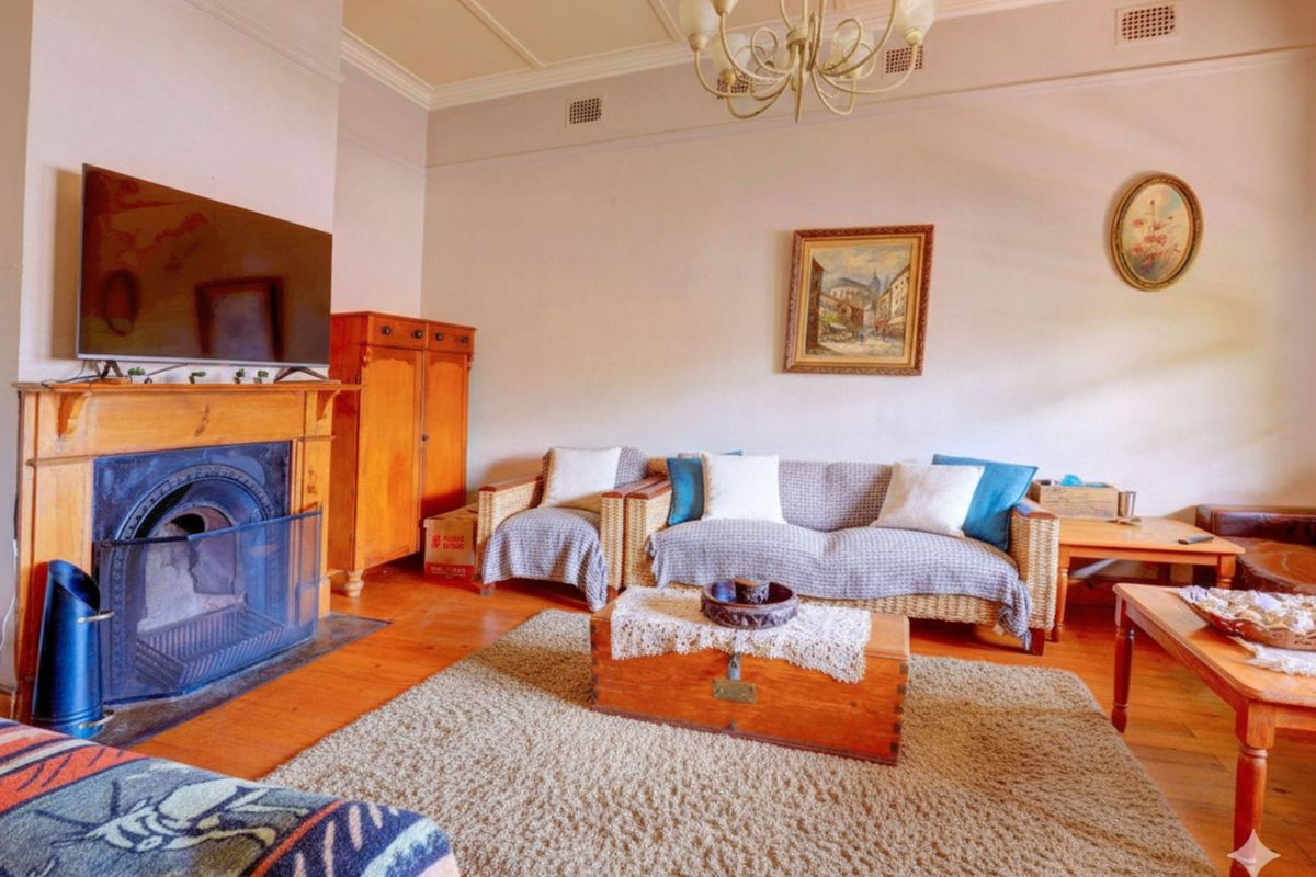 A traditional living room featuring a classic fireplace with a timber mantelpiece, high ceilings with decorative cornices, and polished timber flooring.