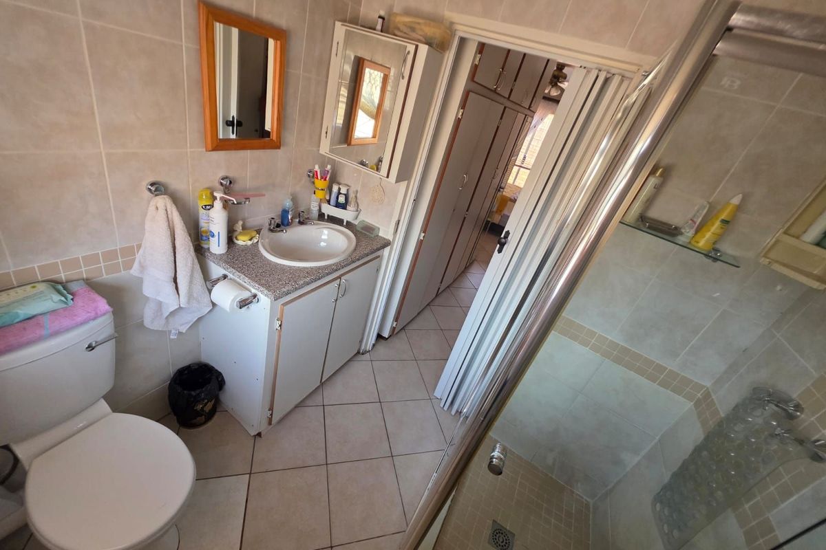 A functional bathroom featuring a vanity with a basin, a toilet, and a glass-enclosed shower, with tiled walls and flooring throughout.