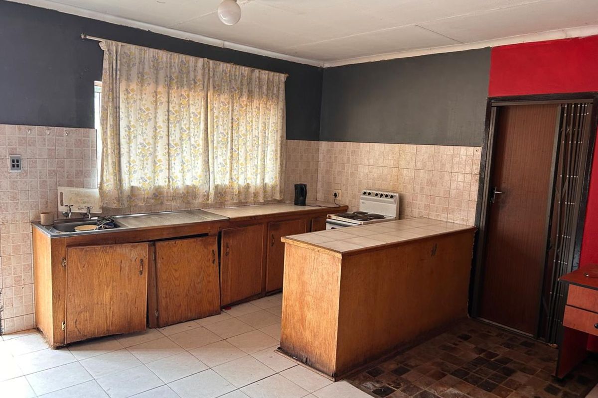 A dated kitchen featuring wooden cabinetry, tiled splashbacks, and a freestanding stove, offering significant potential for modernization and renovation.