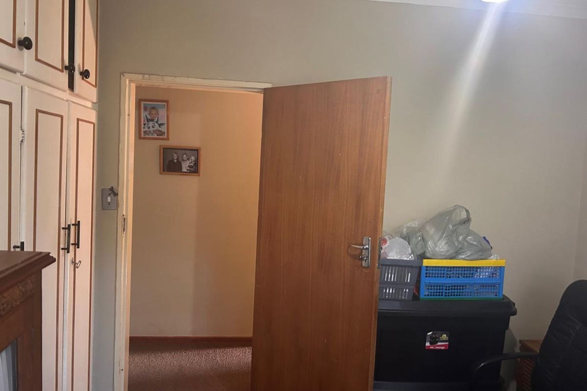 A bedroom featuring built-in cupboards and a doorway leading to an adjacent room, showing signs of wear on the ceiling and finishes.