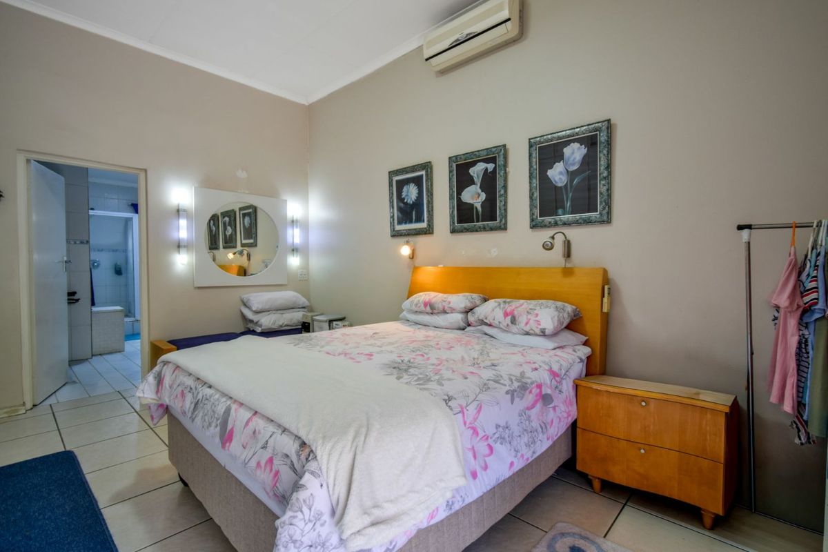 A bedroom featuring tiled flooring, a wall-mounted air conditioning unit, and an en-suite bathroom access.