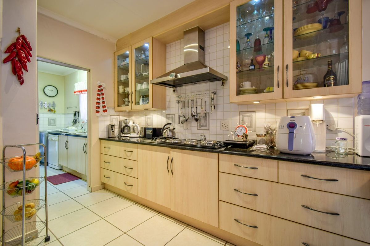 A functional kitchen featuring light wood cabinetry, dark granite countertops, a stainless steel extractor fan, and tiled flooring, with an adjacent scullery area.
