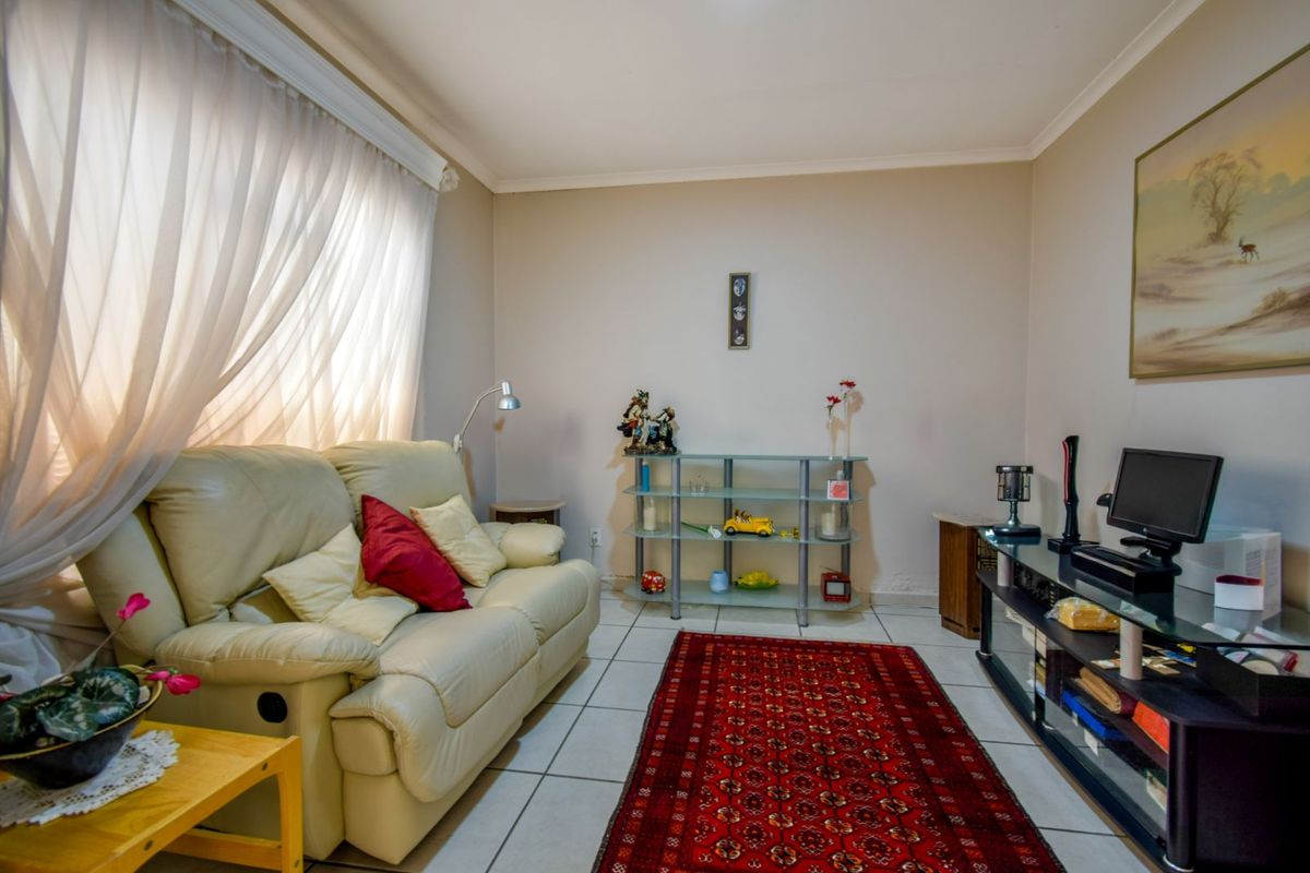 A cozy living room featuring neutral wall tones, tiled flooring, and large windows with sheer curtains, providing a comfortable and functional living space.
