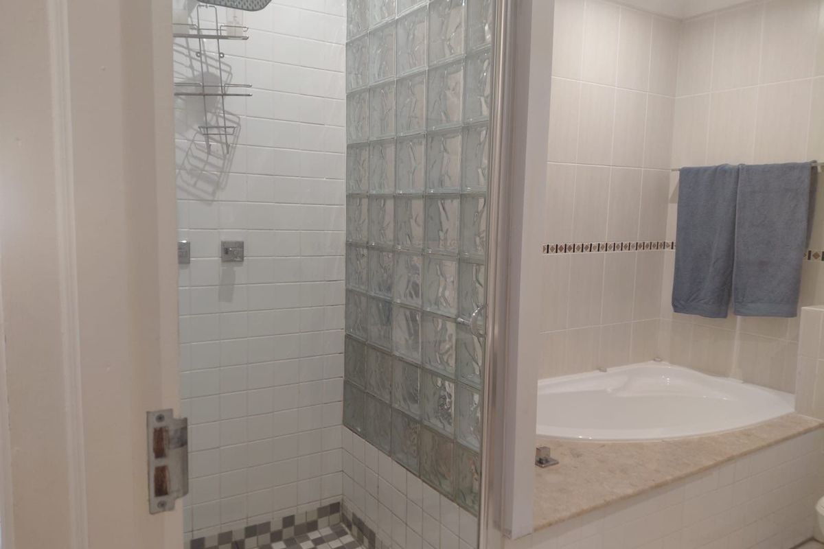 A bathroom featuring a separate shower enclosure with glass block wall and a built-in bathtub with stone-look surround.
