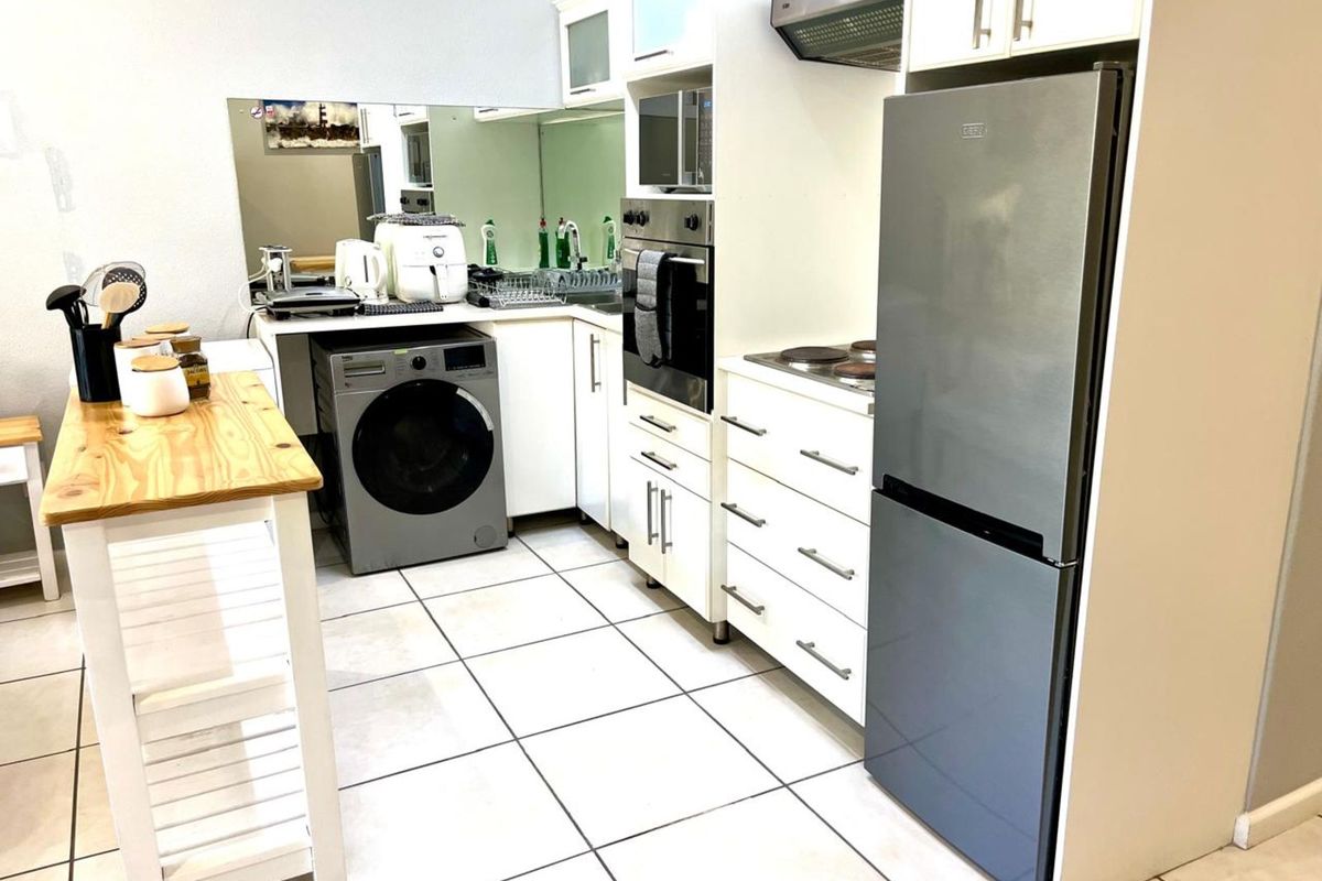 Compact kitchen featuring white cabinetry, built-in oven, extractor fan, tiled flooring, and integrated space for laundry appliances.