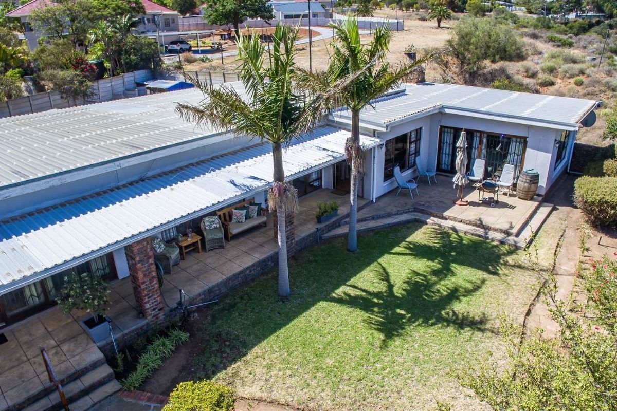 Aerial view of a residential property featuring a large covered patio, brick pillars, and a landscaped garden area with mature palm trees.