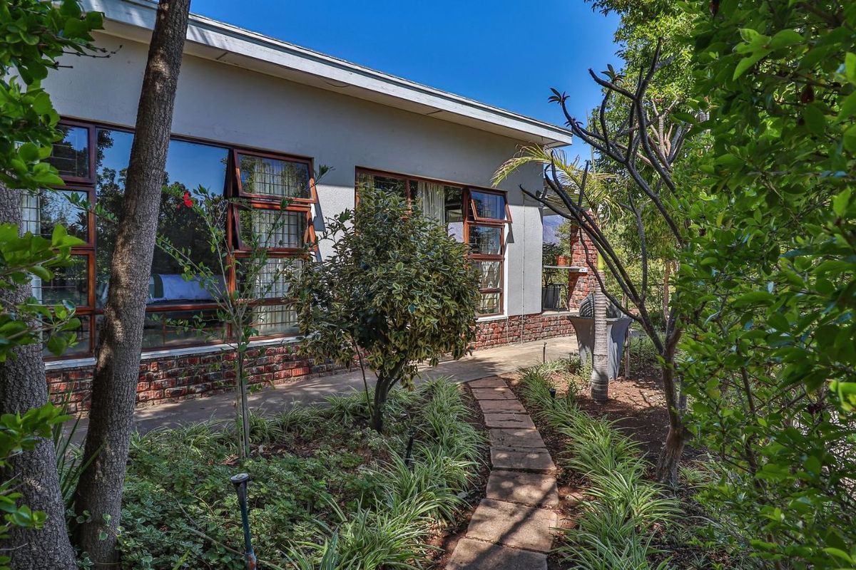 A view of the rear exterior facade featuring large windows, brick base detailing, and a stone pathway leading through the landscaped garden.
