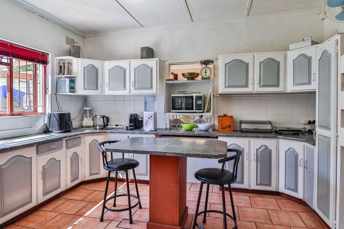 A functional kitchen featuring traditional cabinetry, tiled countertops, and terracotta-style flooring, offering a classic layout with ample storage and preparation space.