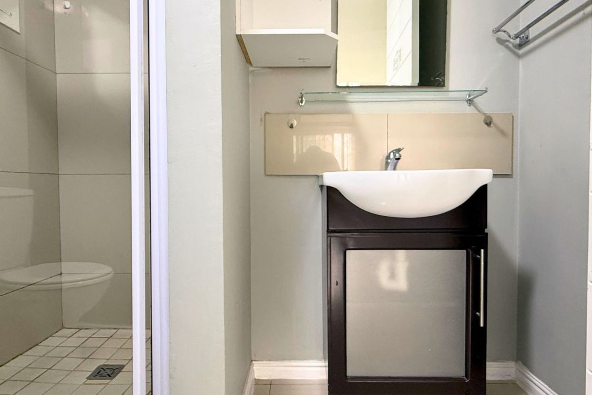 A functional bathroom featuring a vanity with a basin, a wall-mounted mirror, and a separate tiled shower enclosure.