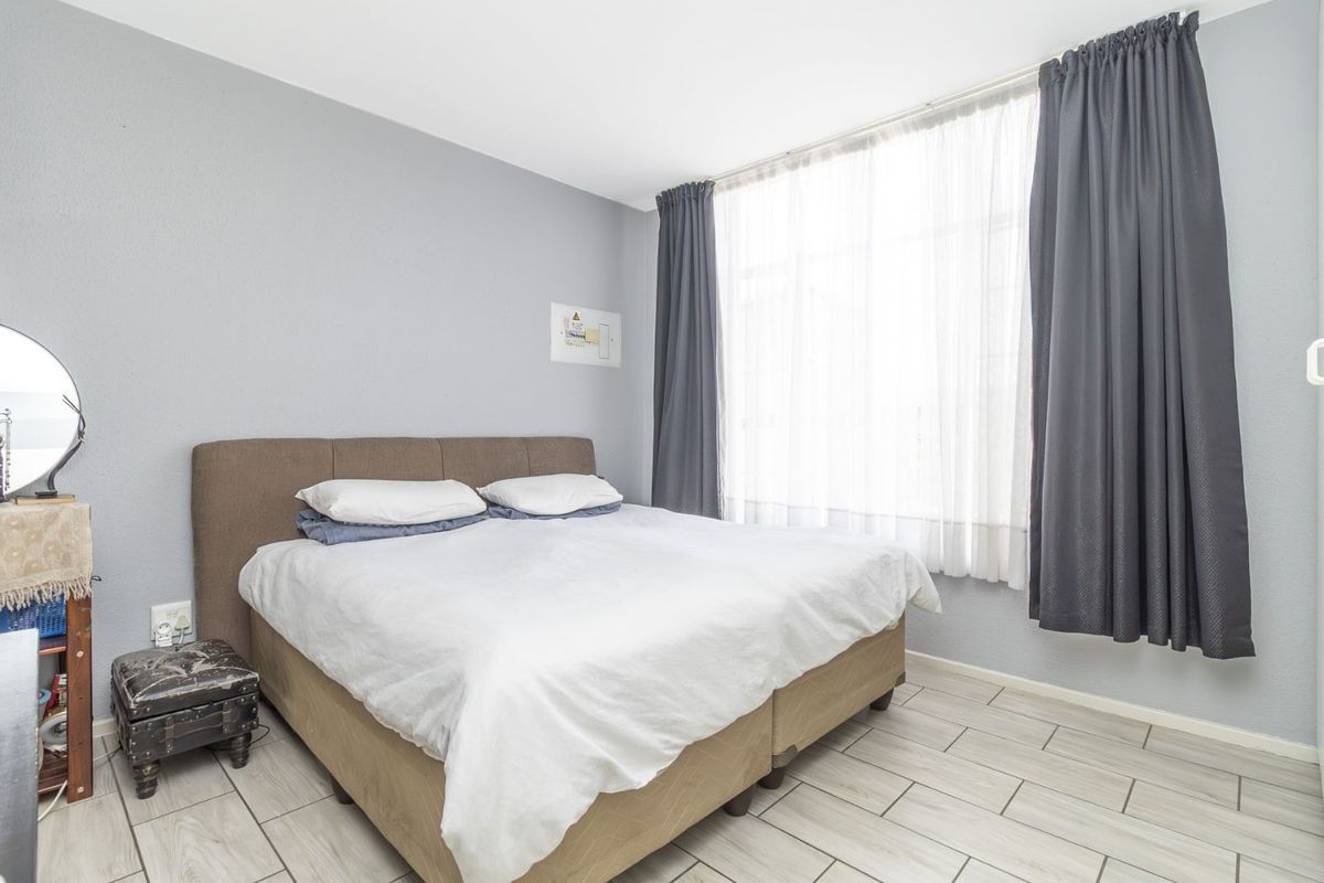 A well-lit bedroom featuring neutral grey walls, tiled flooring, and large windows with floor-to-ceiling curtains.
