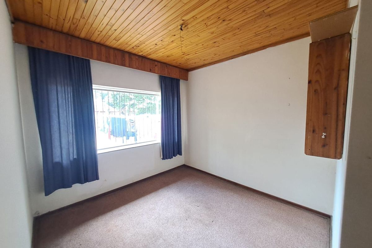 A vacant bedroom featuring a timber-clad ceiling, carpeted flooring, and a window fitted with security bars.
