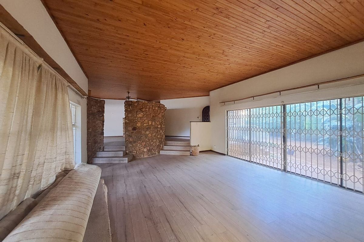 Spacious living area featuring a natural stone feature wall, timber-clad ceiling, and large sliding glass doors with security gates leading to the exterior.