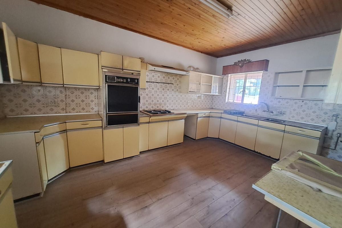 A spacious, dated kitchen featuring original cabinetry, built-in oven, hob, and wood-paneled ceiling, offering significant potential for a modern renovation.