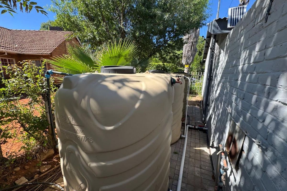 Exterior side passage featuring two large plastic water storage tanks connected to the property's plumbing system.