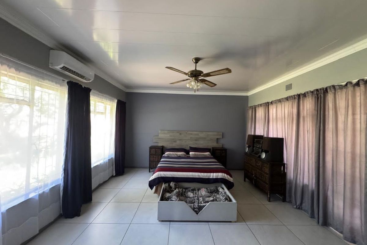 Spacious bedroom featuring large format floor tiles, a ceiling fan, and a wall-mounted air conditioning unit.