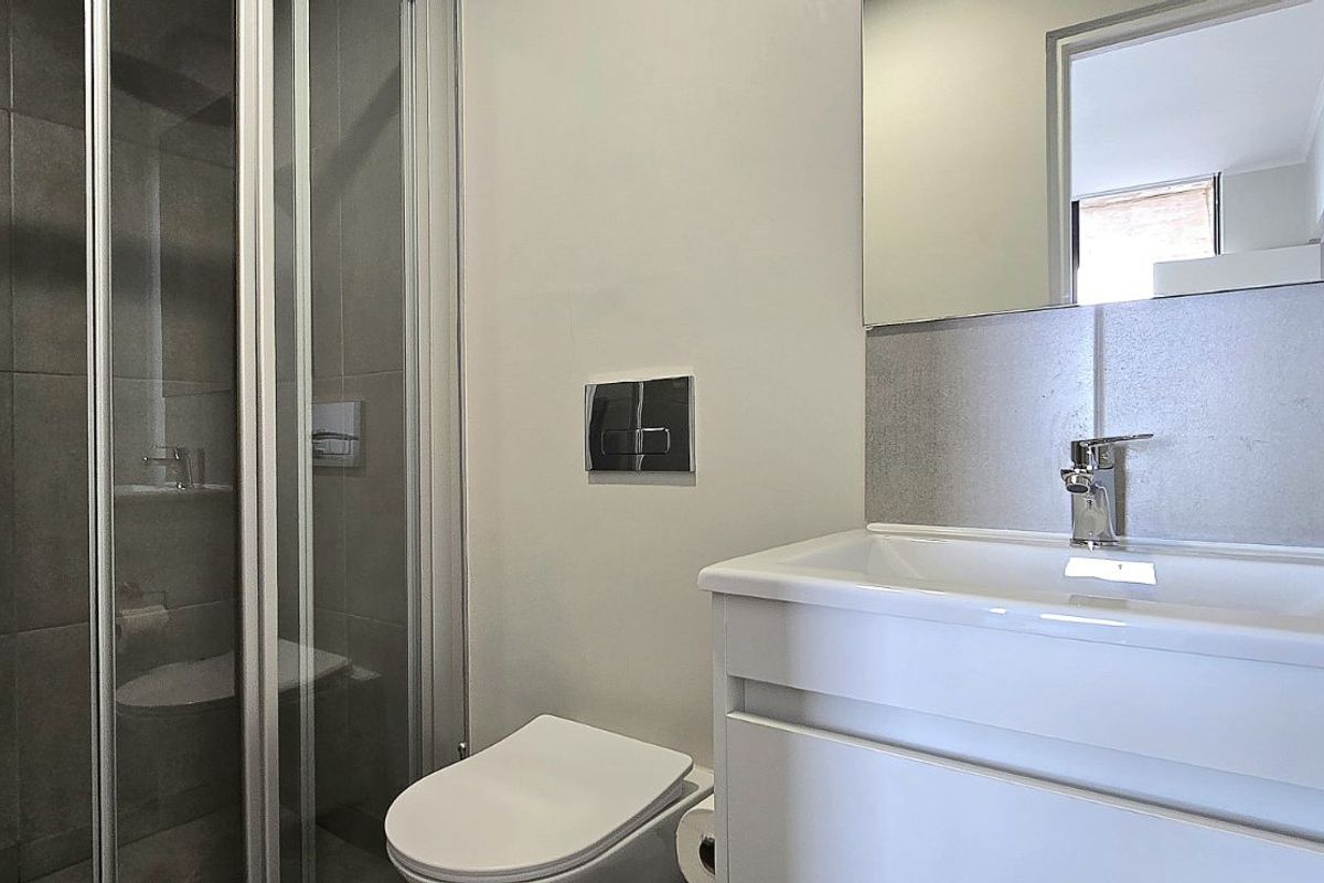 Modern bathroom featuring a glass-enclosed shower with grey tiling, a wall-mounted toilet, and a sleek vanity with a basin and mirror.