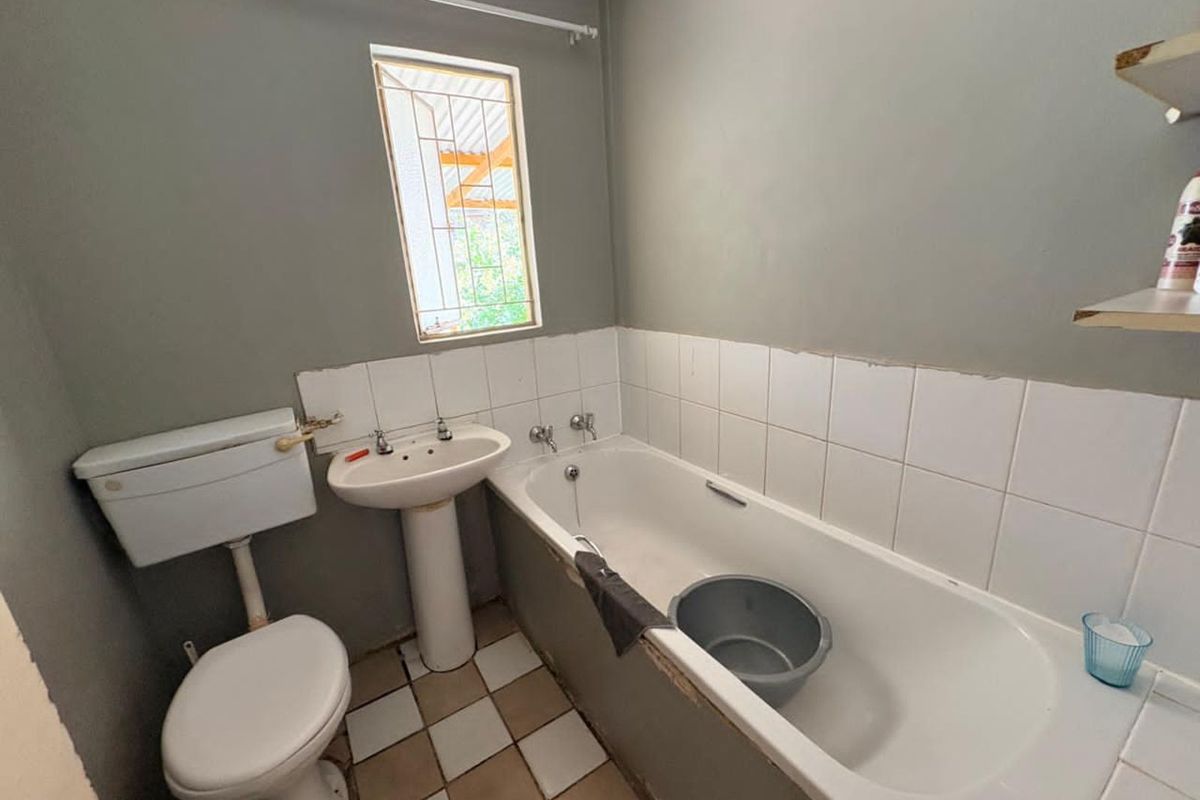 A functional bathroom featuring a standard bathtub, pedestal basin, and toilet with tiled splashbacks and a security-barred window.