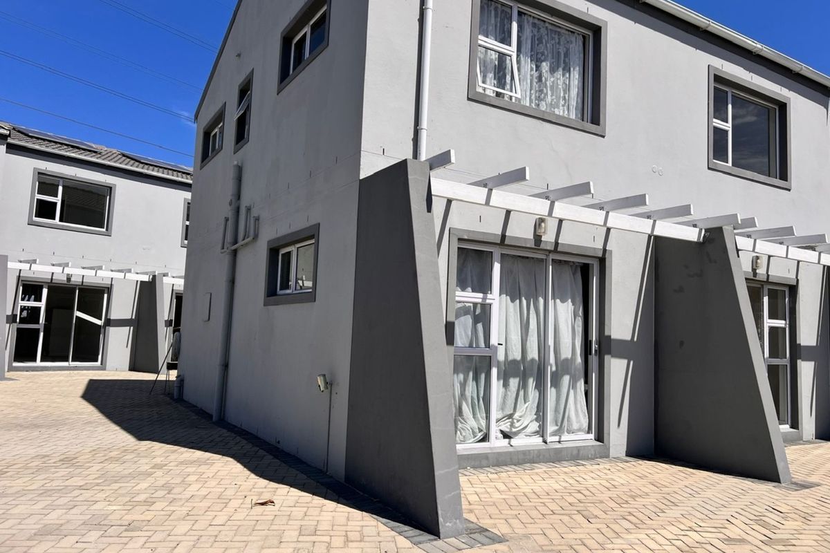Rear view of a modern two-story townhouse featuring a paved courtyard, pergola structure, and sliding glass door access.
