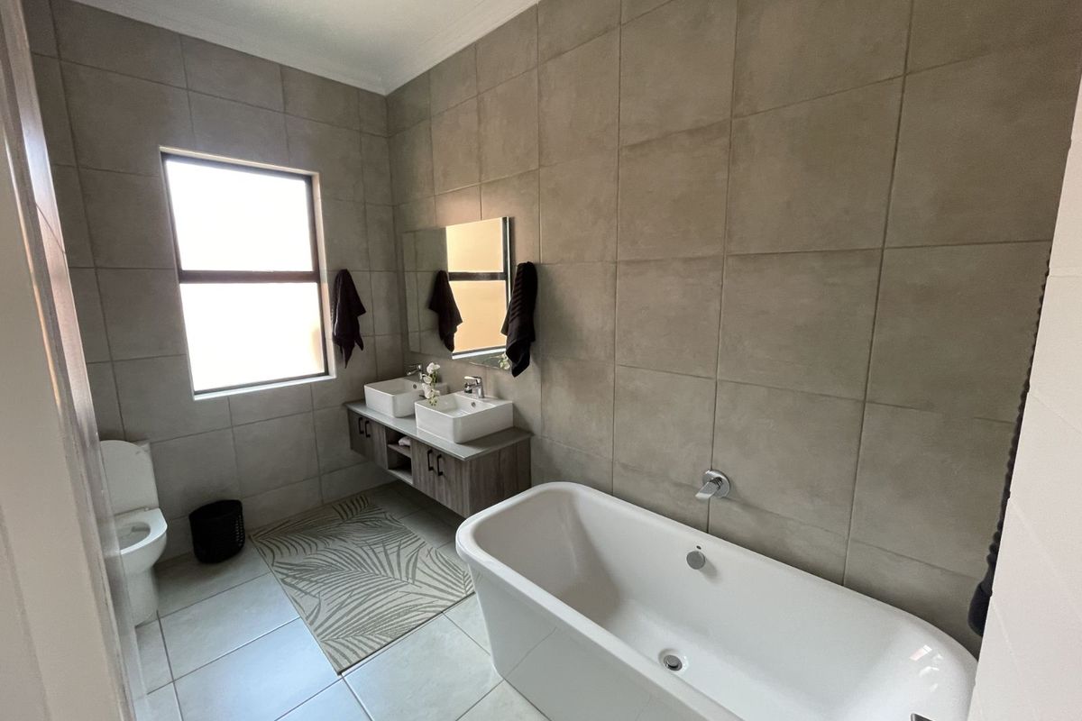 Modern bathroom featuring a freestanding bathtub, double vanity with vessel sinks, and floor-to-ceiling neutral wall tiling.