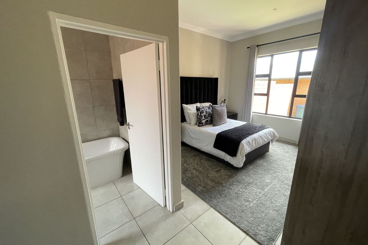 A well-lit bedroom featuring an en-suite bathroom with a modern freestanding bathtub and large windows providing natural light.