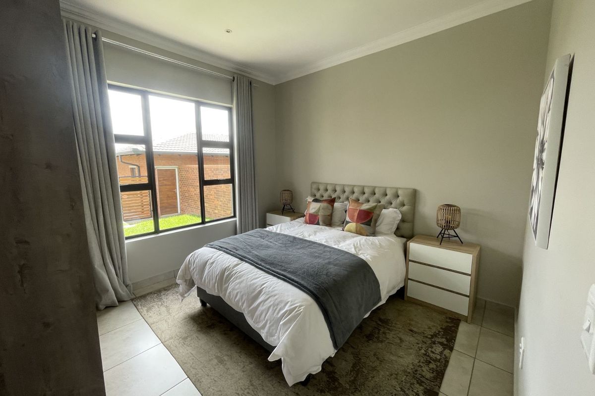 A well-maintained bedroom featuring neutral wall tones, tiled flooring, and large windows that provide natural light and a view of the exterior.