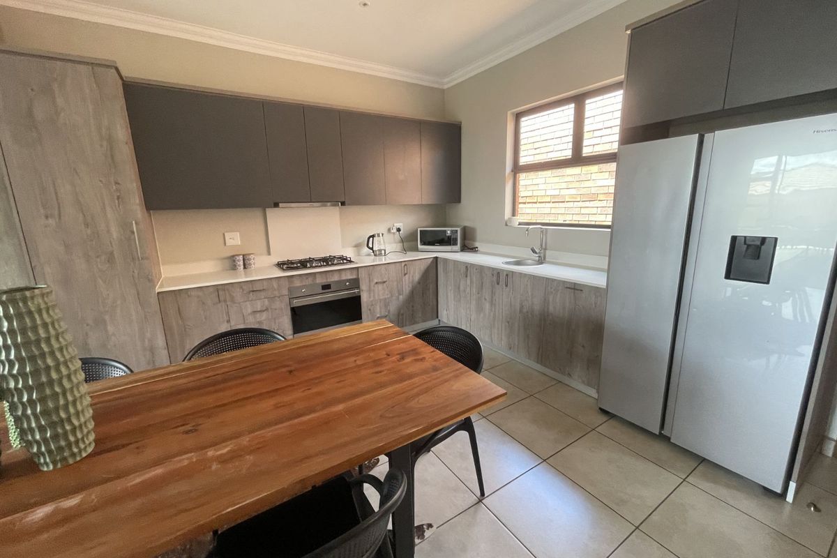 Modern kitchen featuring two-tone cabinetry, stone countertops, built-in oven, gas hob, and extractor fan, with tiled flooring and ample natural light.