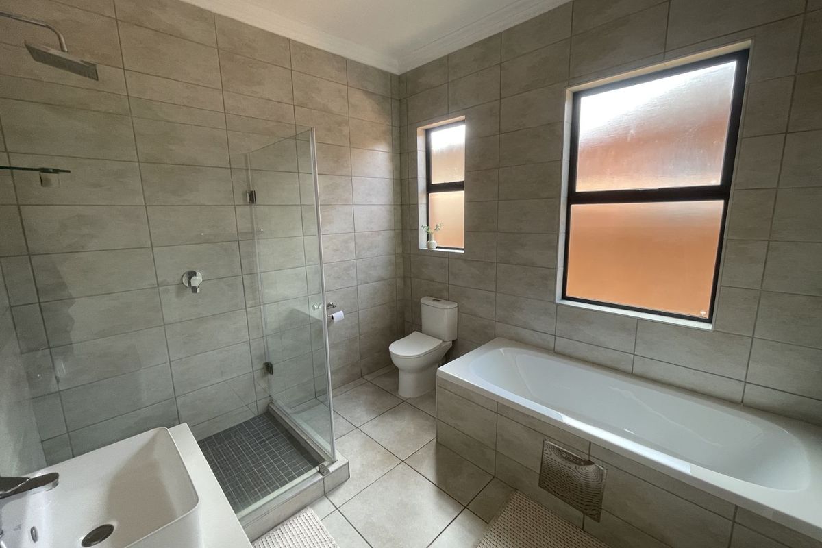 Modern bathroom featuring a glass-enclosed shower, a built-in bathtub, a vanity basin, and a toilet with neutral floor-to-ceiling tiling.