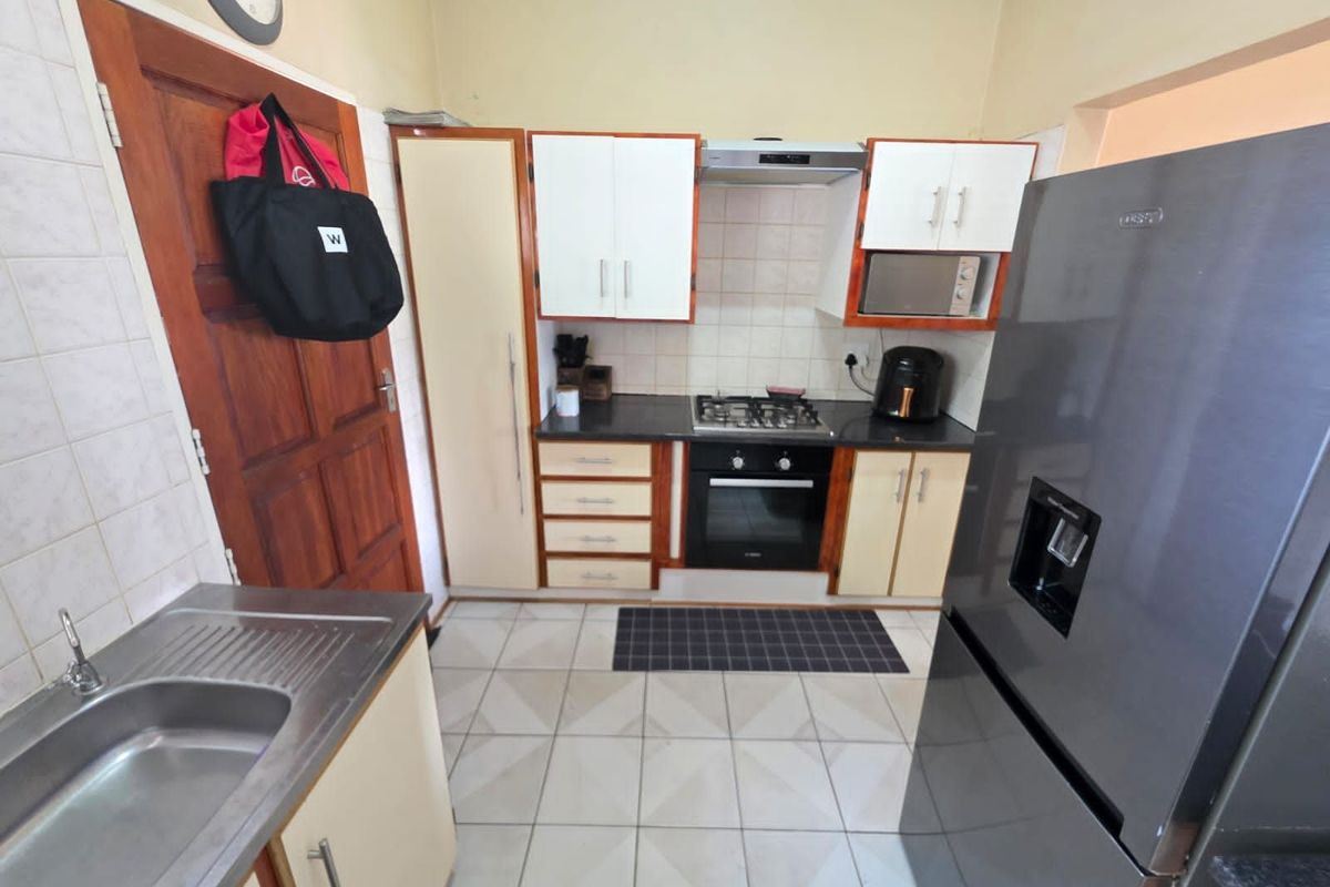 Compact kitchen featuring built-in cabinetry, stainless steel sink, gas hob, oven, and extractor fan with tiled flooring.