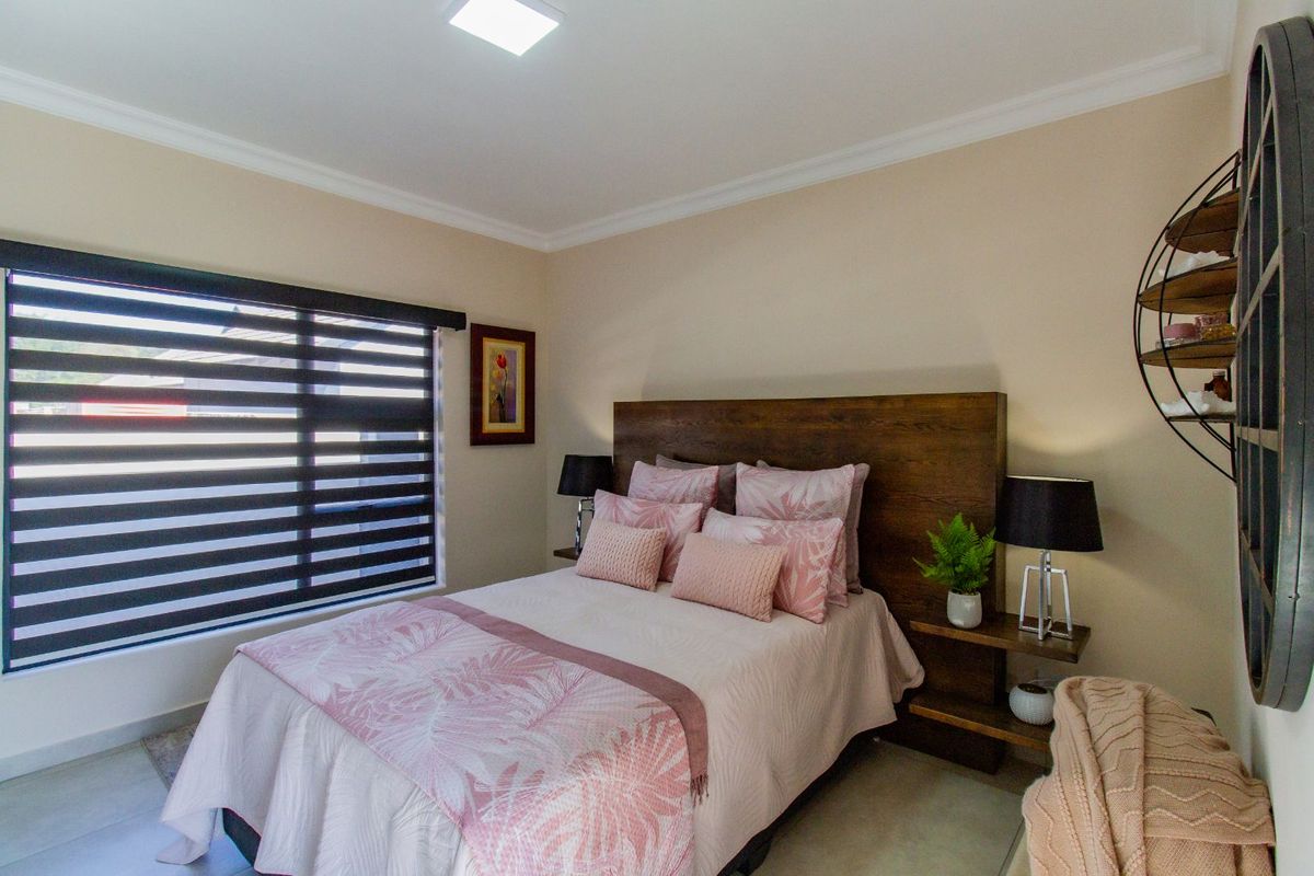 A well-maintained bedroom featuring neutral wall tones, tiled flooring, crown molding, and a large window with modern zebra blinds.