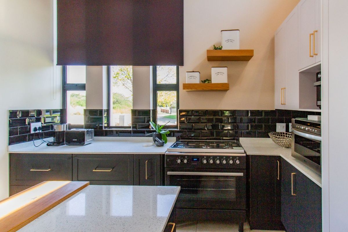 Modern kitchen featuring dark cabinetry, contrasting white stone countertops, black subway tile backsplash, and a built-in gas stove with oven.