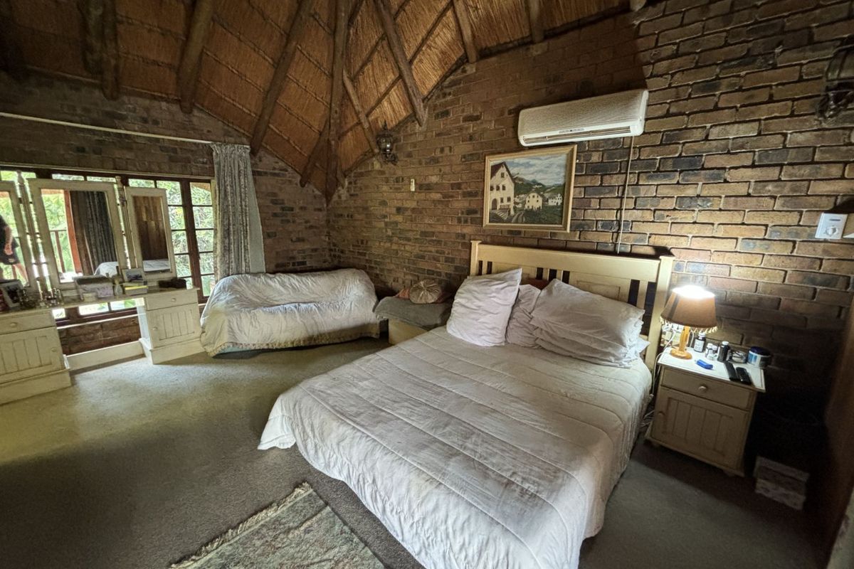 Spacious bedroom featuring a high vaulted thatched ceiling, exposed brick walls, and a wall-mounted air conditioning unit.