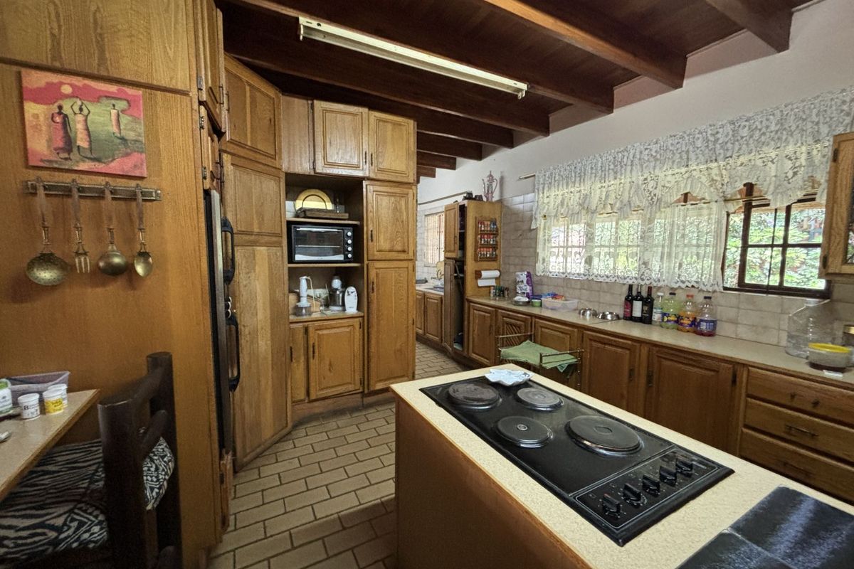 A spacious kitchen featuring extensive wooden cabinetry, a central island with a built-in electric hob, and exposed timber ceiling beams.
