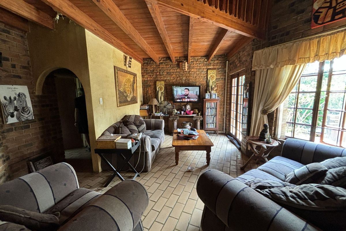 A rustic living room featuring exposed brick walls, vaulted timber beam ceilings, and tiled flooring with large windows providing natural light.