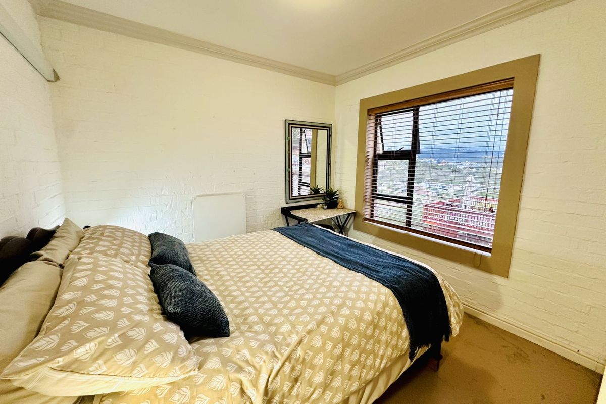 A cozy bedroom featuring painted brick walls, carpeted flooring, and a window with integrated blinds offering an elevated view.